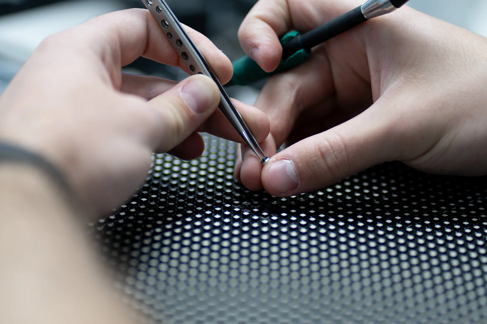 Technician using tweezers and a screwdriver to remove a small component from an LED display module.