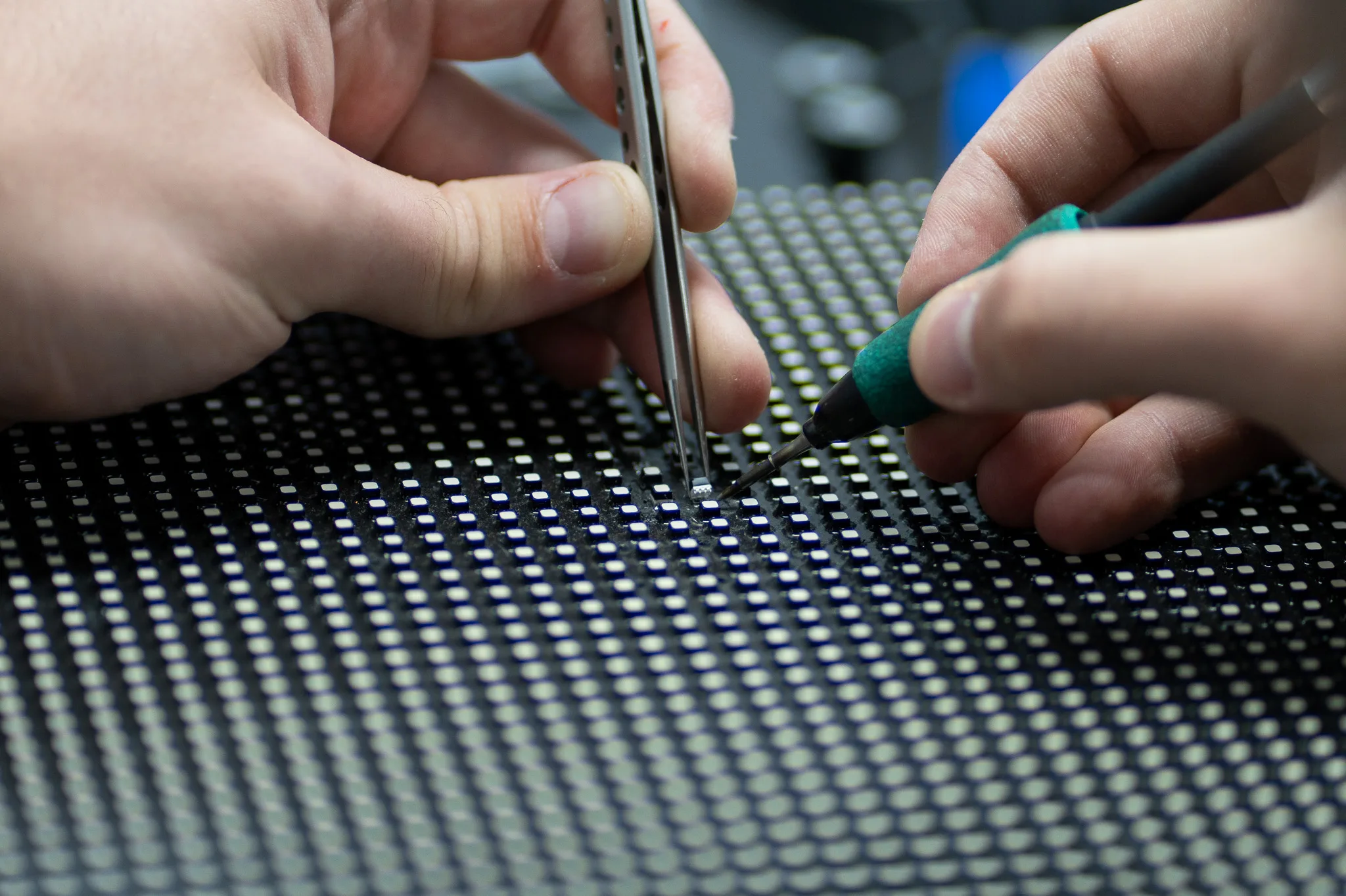 Technician using tweezers and a soldering iron to repair an individual LED on a display module