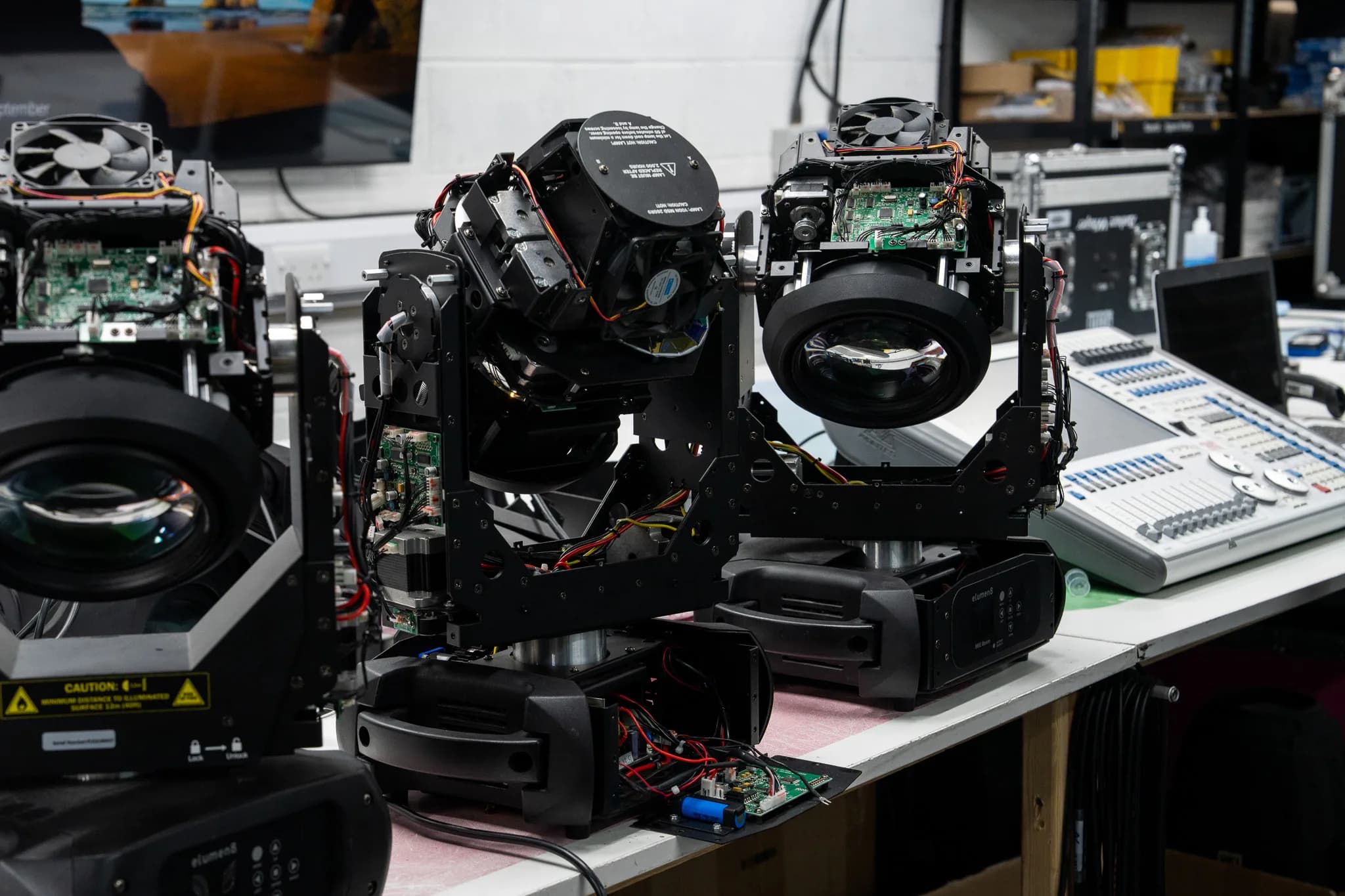 Disassembled moving light fixtures with exposed circuit boards and lenses on a repair workbench