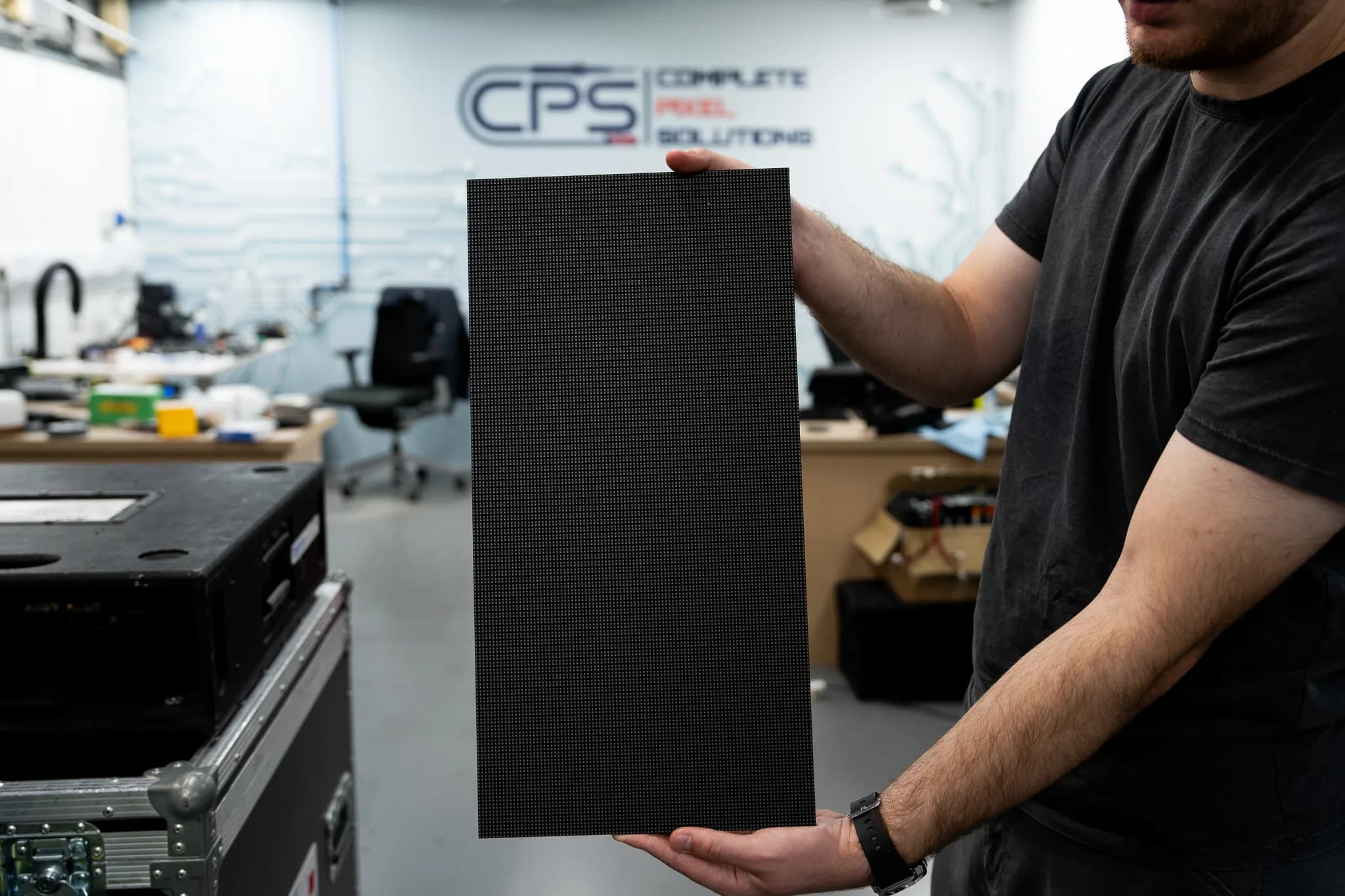 CPS technician holding an LED display panel in the workshop, the CPS logo on the wall behind