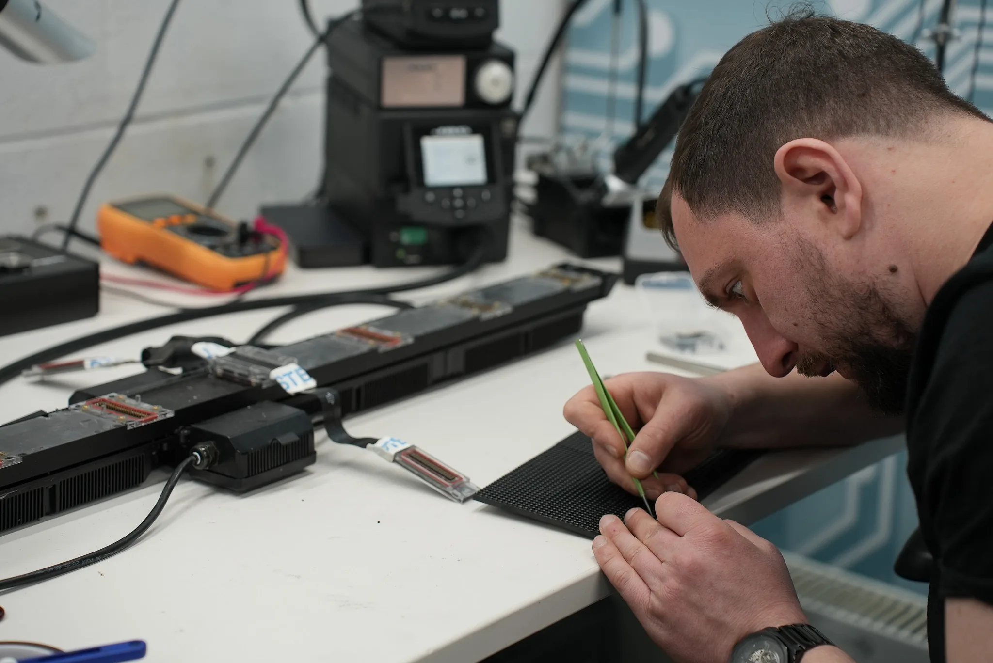 Technician at the bench working on an LED panel receiving card with a fibre pen, test equipment nearby
