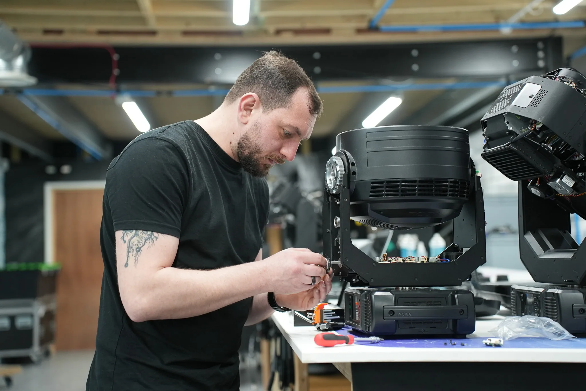 CPS technician servicing an opened Robe moving head at the workshop bench, with more fixtures waiting behind