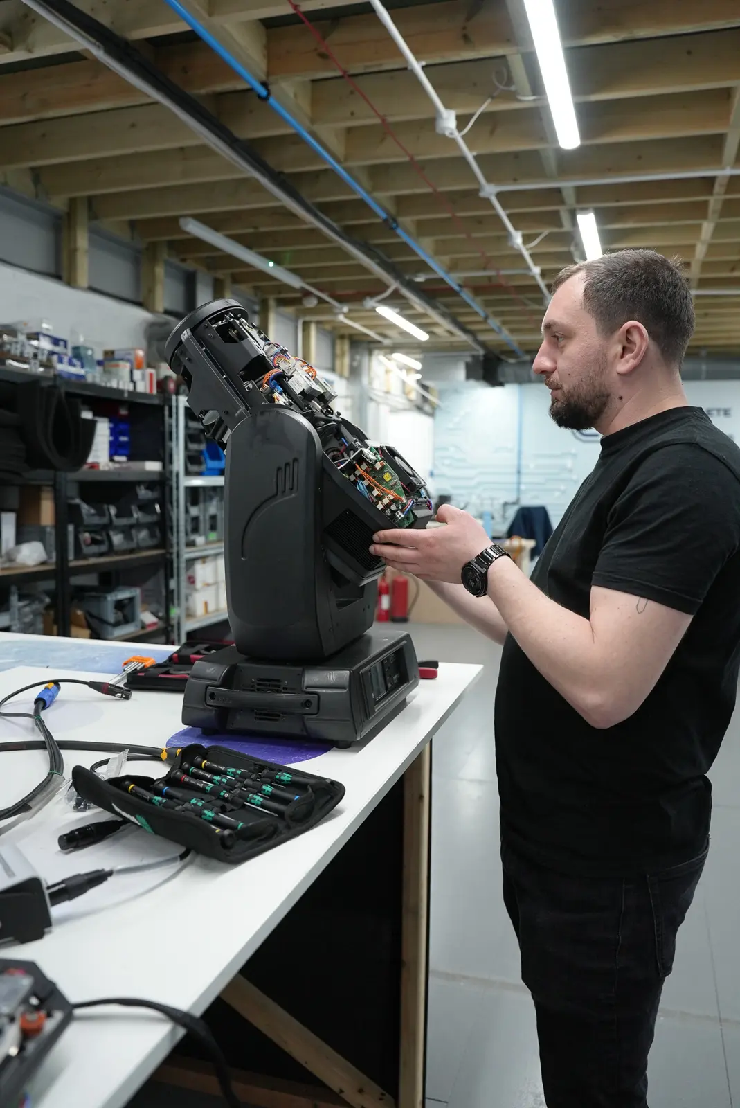 Technician inspecting the open internal components of a moving head light on a workbench